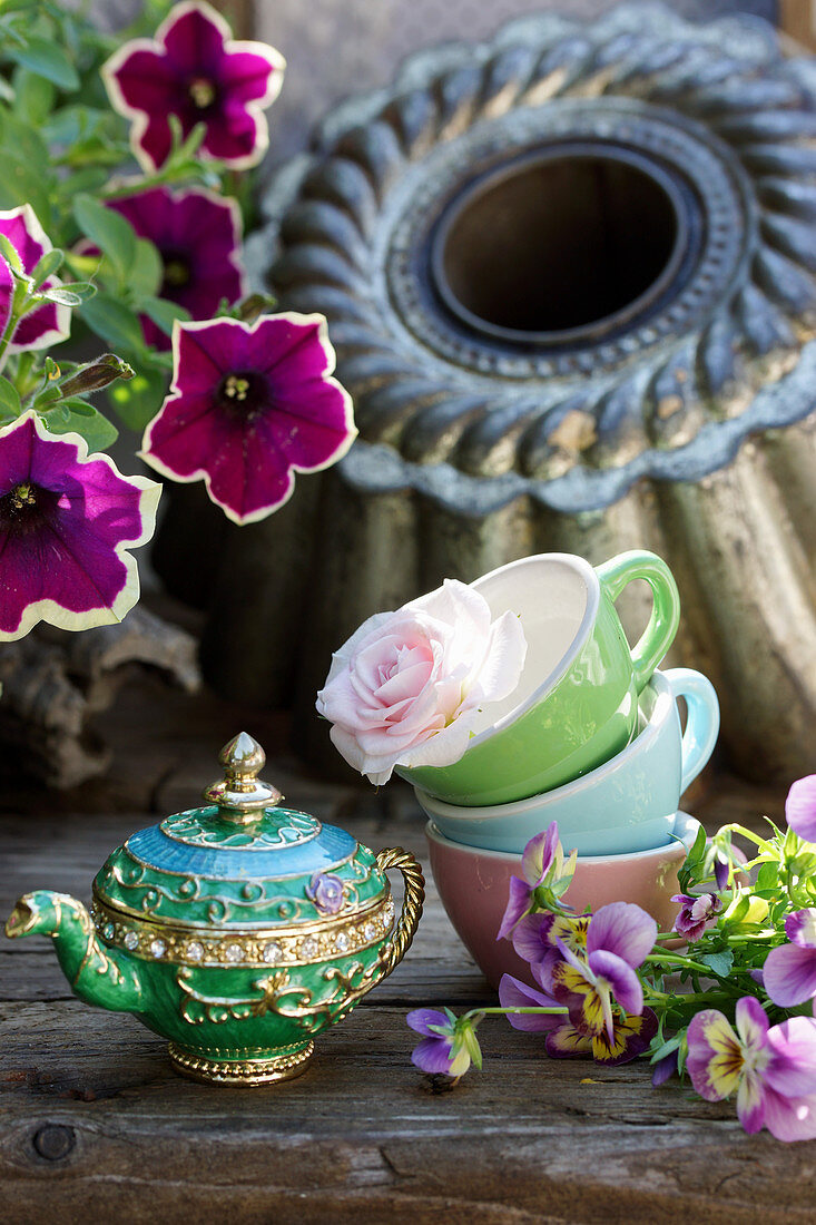 Teapot next to rose in cups, petunias and violas
