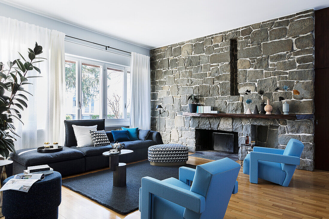 Light blue designer armchairs and sofa in living room with stone wall