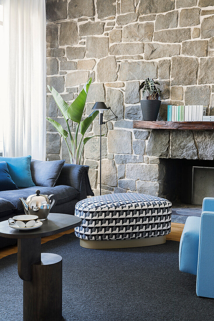 Side table, pouffe and sofa in front of stone wall in living room