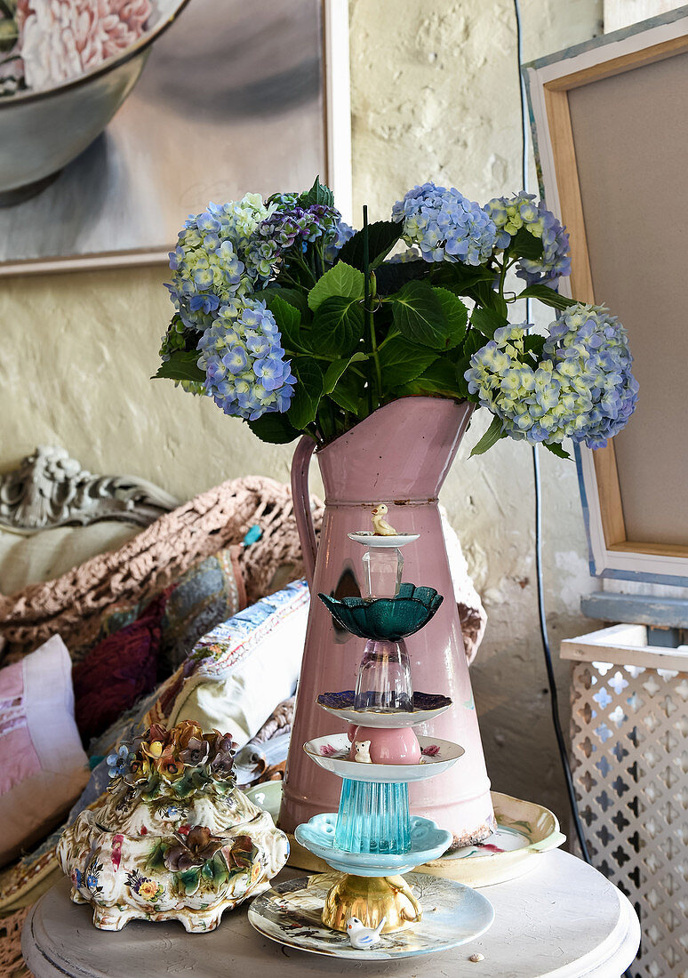 Etagere aus gestapelten Tassen vor Blechkanne mit blauen Hortensien