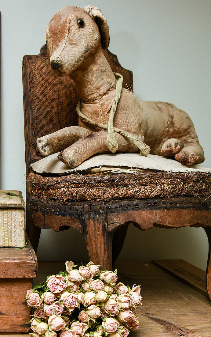 Antikes Stofftier auf altem Stuhl und getrockneter Rosenstrauß