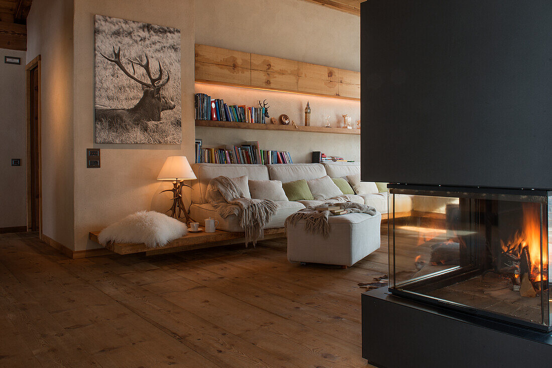 Comfortable sofa below wooden shelves in cosy living room with fireplace in foreground