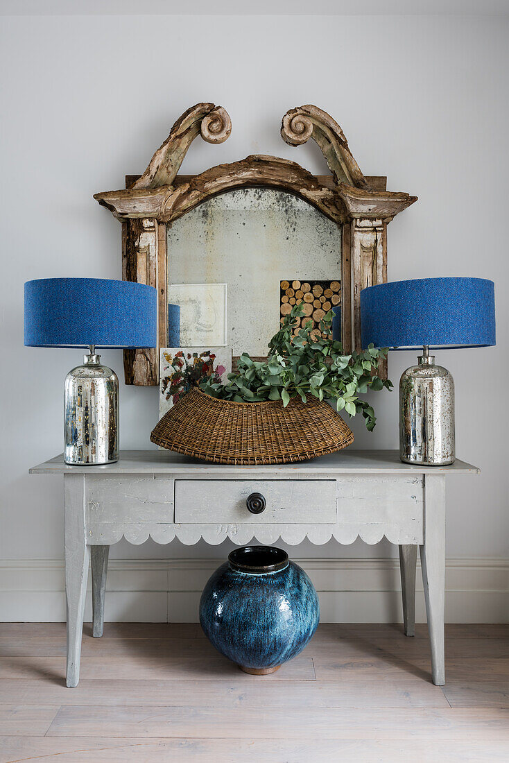 Two table lamps and planted basket on console table belowa ntique mirror