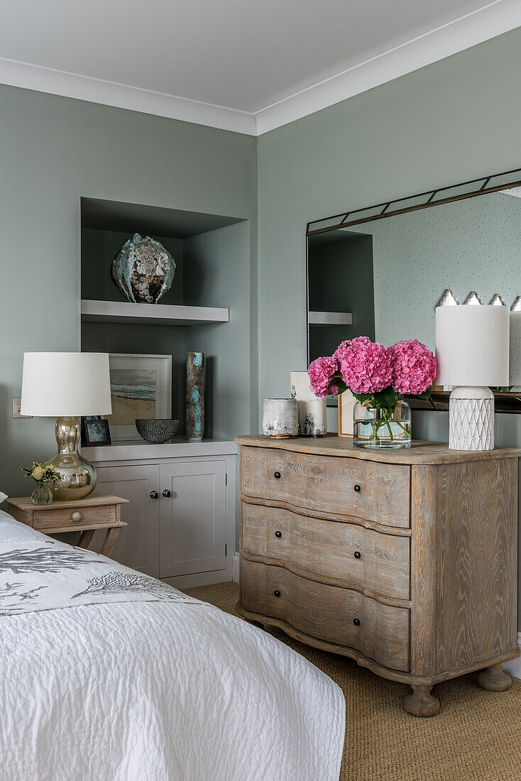Wooden chest of drawers and fitted shelf in bedroom with sage-green walls