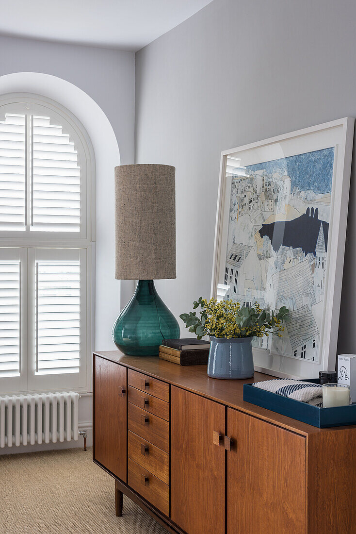 Table lamp, bouquet of flowers and modern artwork on sideboard