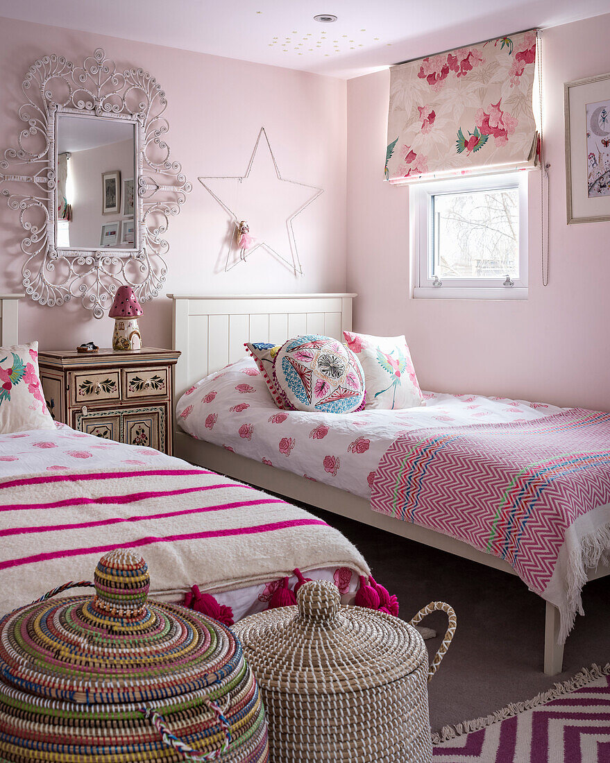 Zwei Einzelbetten und Wäschekörbe im rosafarbenen Zimmer mit floralem Raffrollo