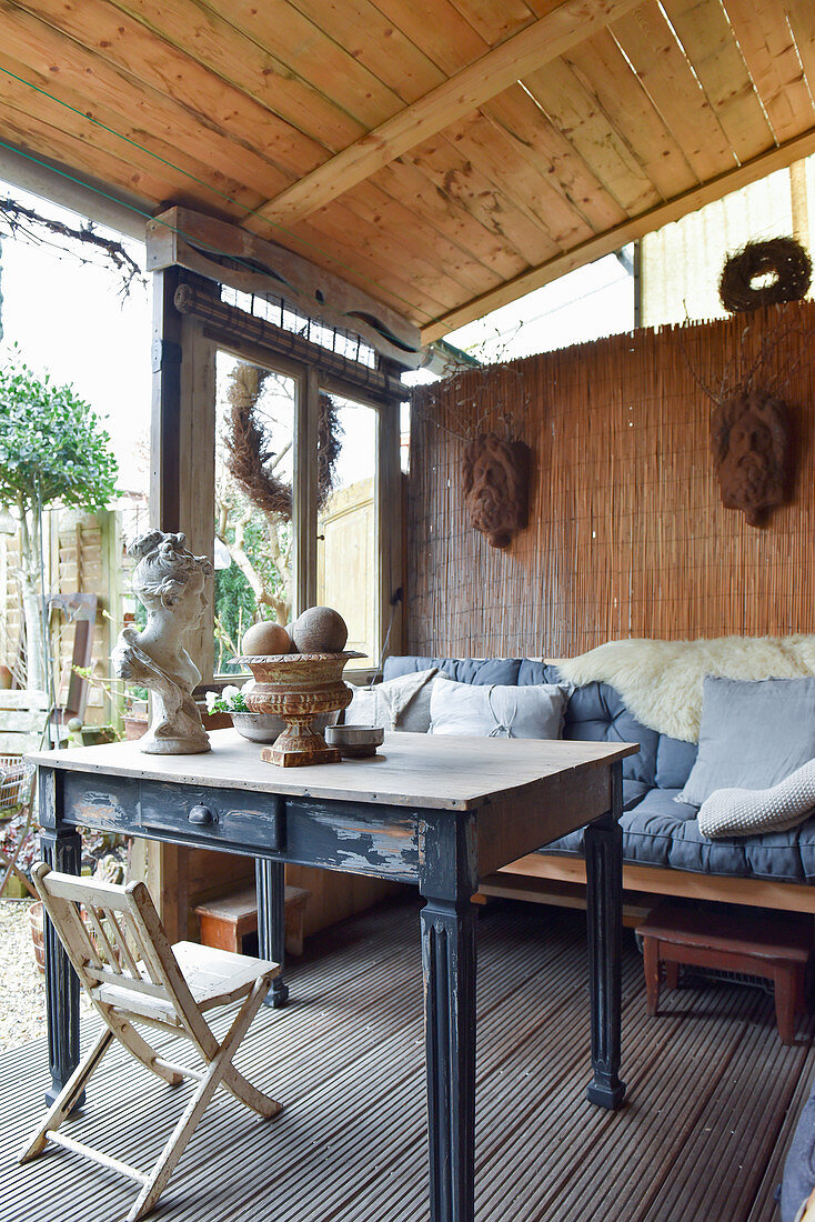 Alter Tisch und Bank auf überdachter Terrasse mit Vintage-Deko