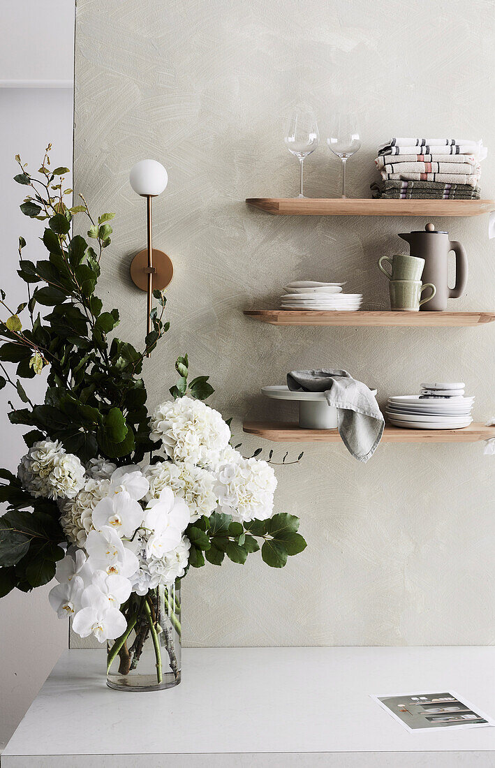 Holzregale mit Geschirr an der Wand, Strauß aus weißen Blumen auf Tisch