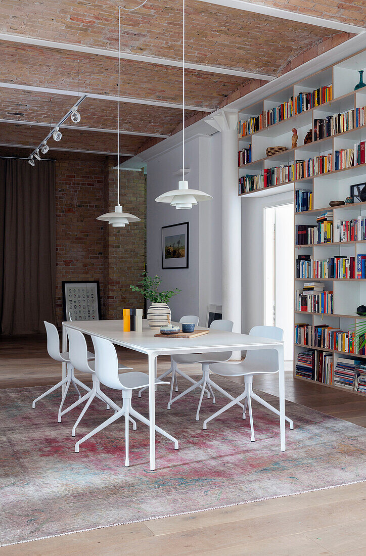 Eßtisch mit Stühlen, darüber Pendelleuchte und Bücherwand in offenem Wohnraum mit hoher Decke