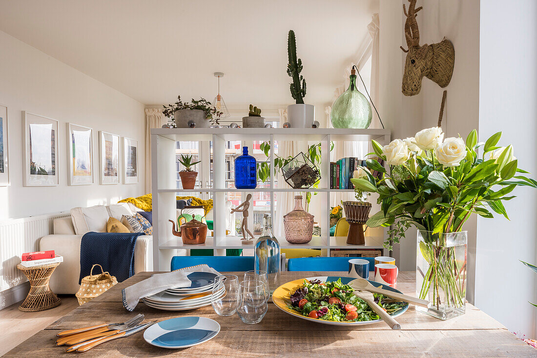 Salatplatte, Geschirr und Blumenstrauß auf Esstisch vor offenem Raumteiler-Regal