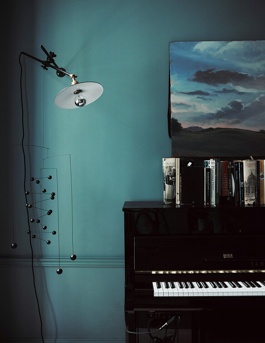 Black piano and lamp in front of petrol-coloured wall