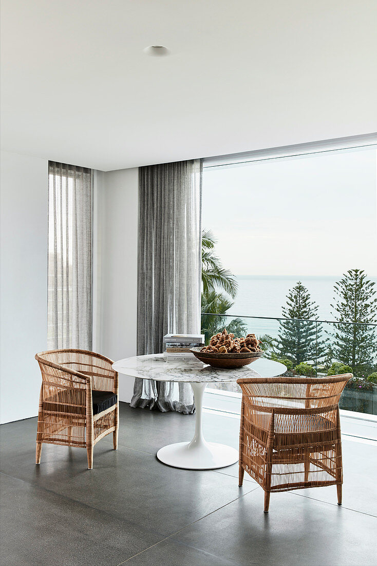 Two wicker armchairs at designer table in front of balcony with panoramic view