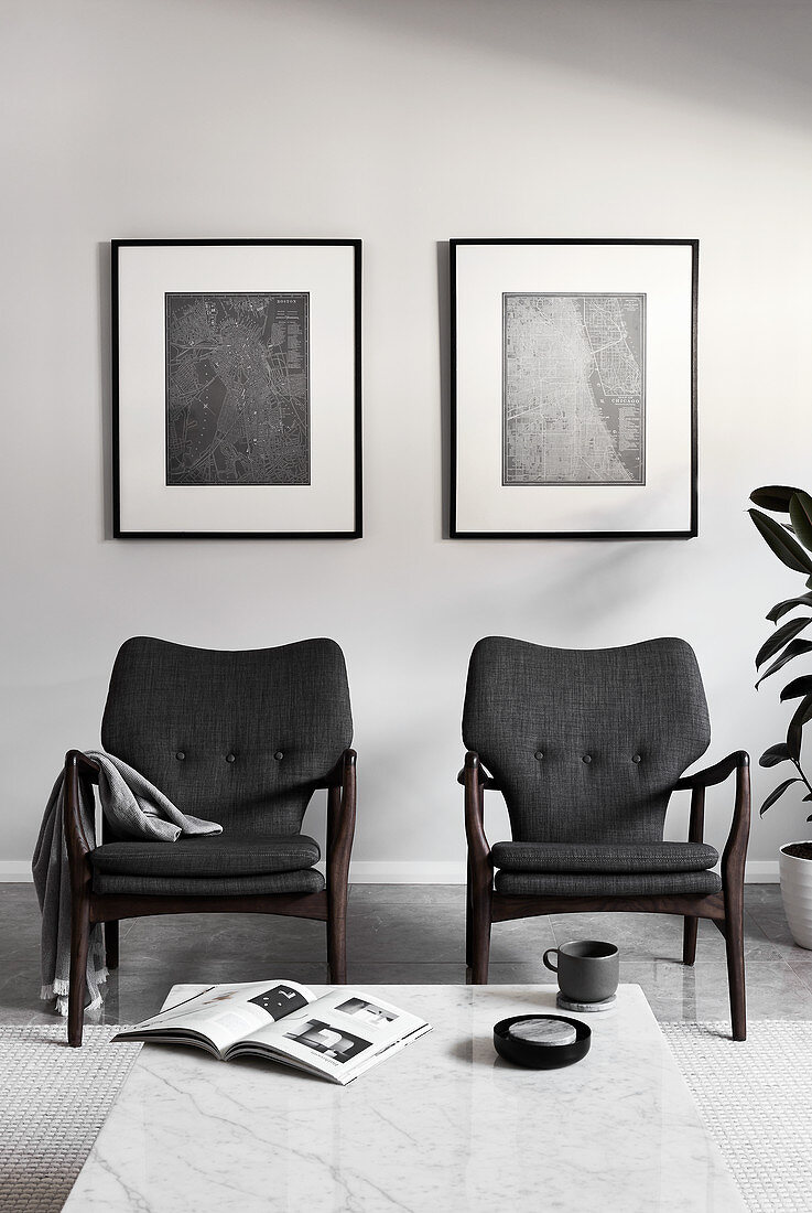 Two grey armchairs below monochrome artworks on wall in living room