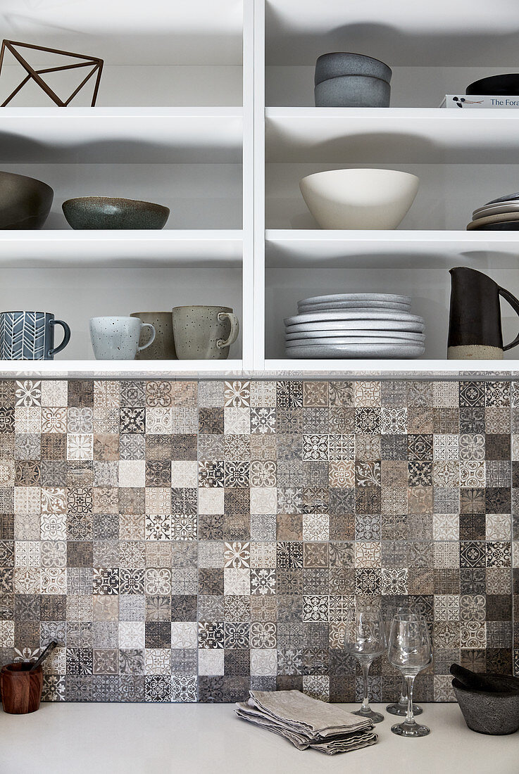 Stoneware crockery on kitchen shelves above mosaic-tiled splashback
