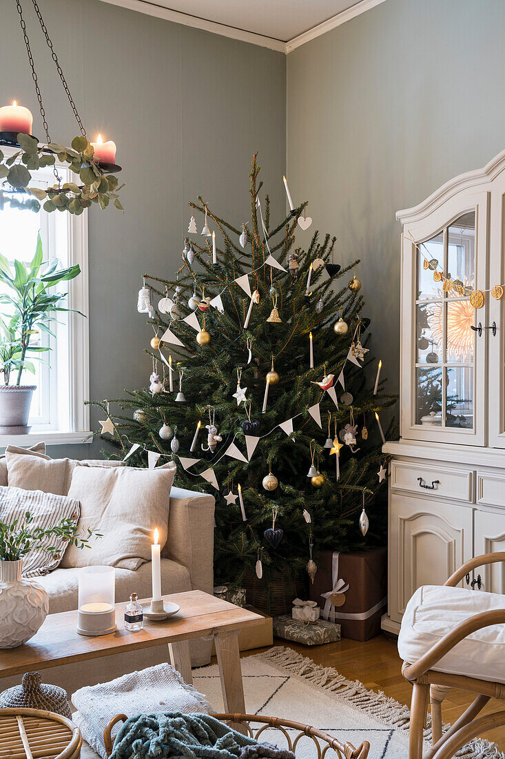 Christmas tree between sofa and glass-fronted cabinet in living room