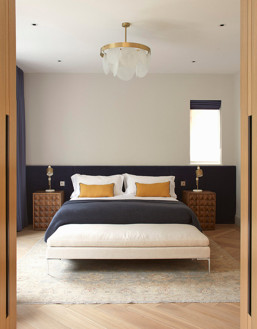 View into symmetrical bedroom with half-height, dark blue panel behind bed