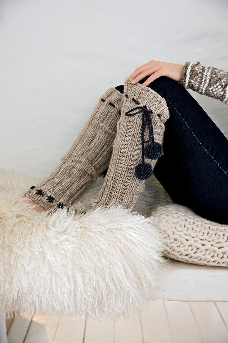 Woman wearing knitted leg warmers sitting on knitted cushion