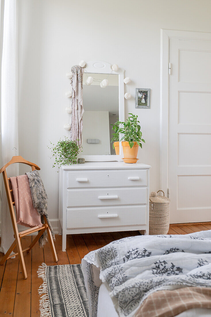 White chest of drawers with a mirror and clothes rack in a corner of the bedroom