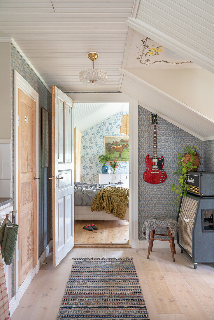 Flurbereich mit nostalgischer Tapete und Dachschräge, Gitarre neben offener Tür an der Wand, Blick ins Schlafzimmer
