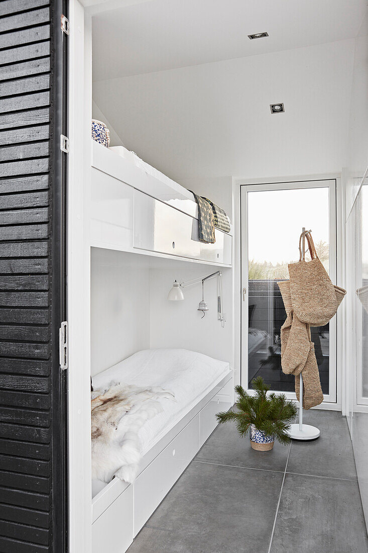 White bunk bed, spruce branches and coat rack in a narrow bedroom