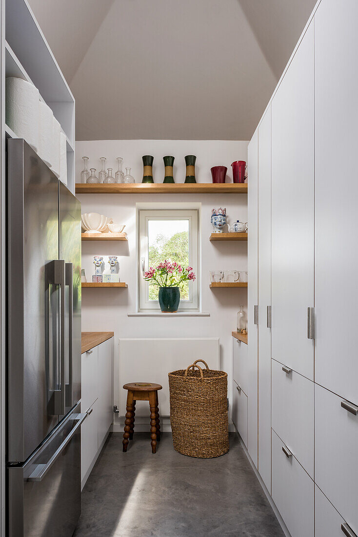 Schmale Küche mit weißen Schränken, Regalen und Kühlschrankkombination
