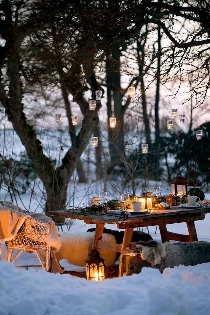 Hängende Laternen am Baum über gedecktem Tisch in verschneitem Garten
