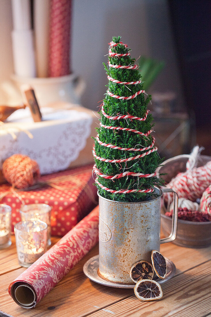 Mini Christmas tree wrapped with red and white thread in a zinc jar