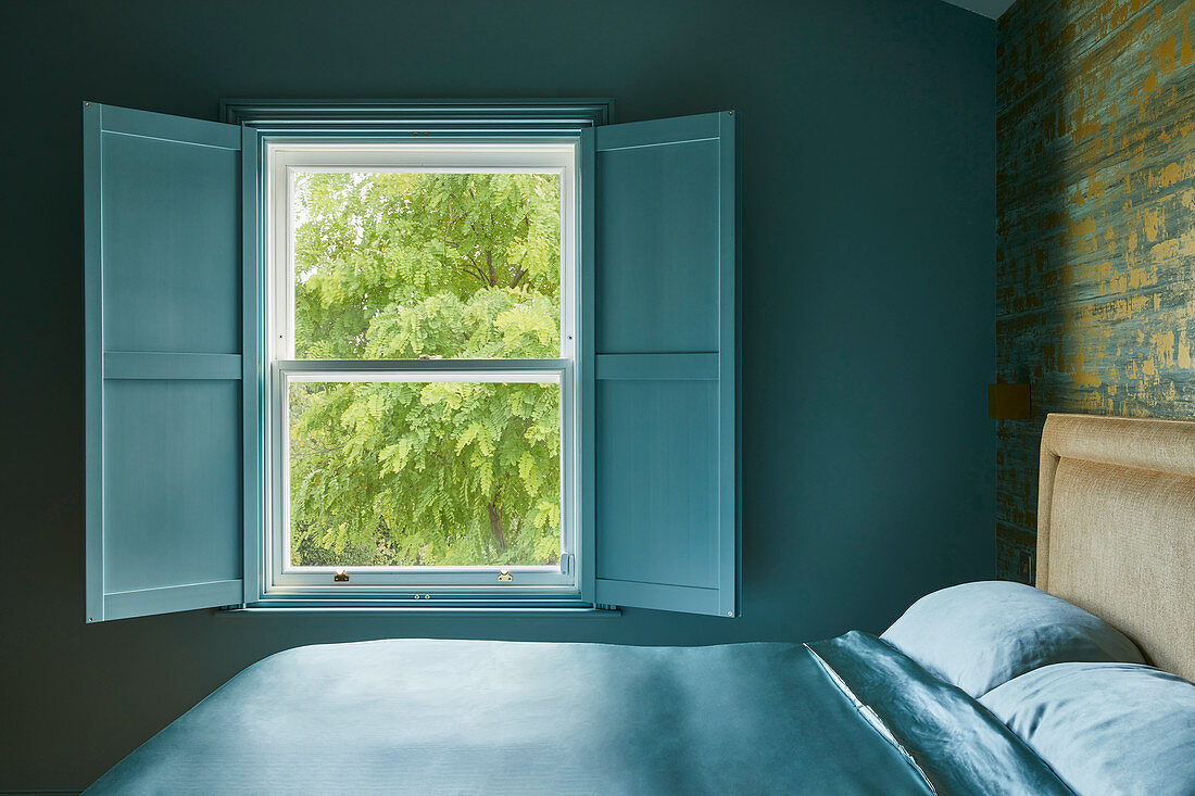 Doppelbett und geöffnete Fensterläden im Schlafzimmer mit blauer Wand