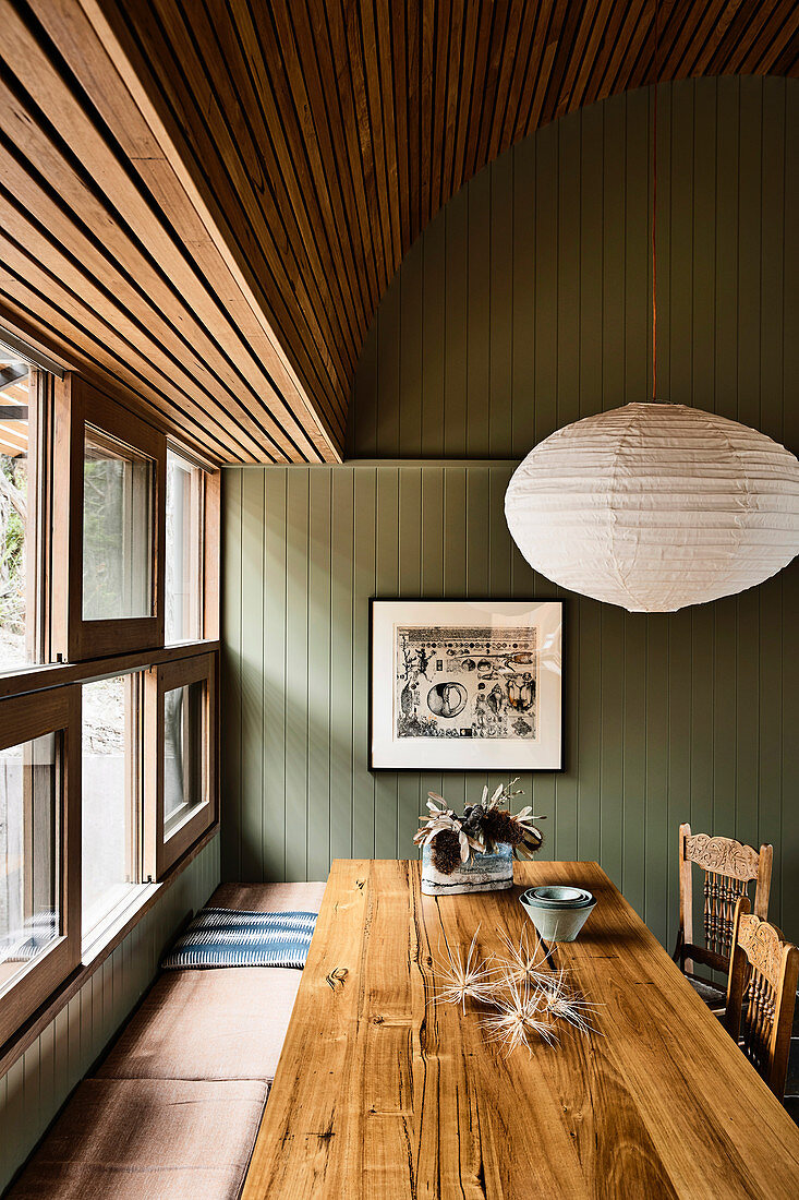 Dining table and bench below window in kitchen with green wood panelling