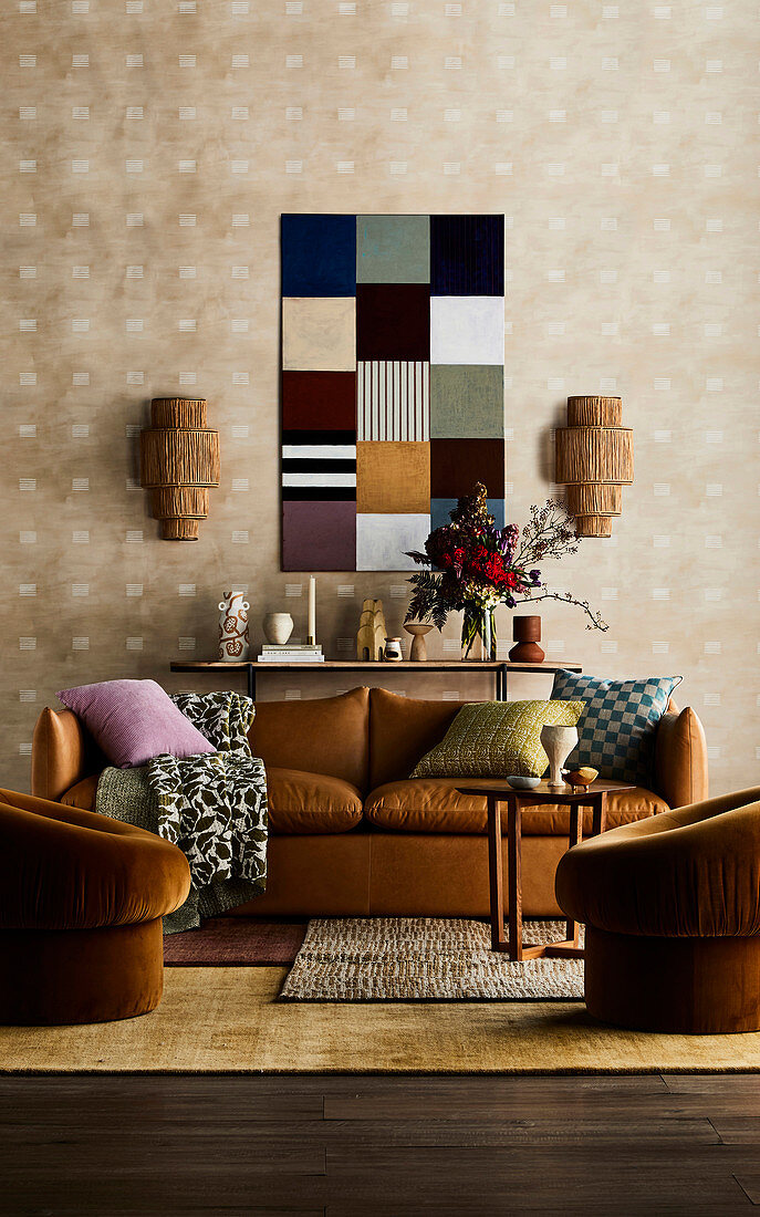Brown leather couch with cushions, console behind, wall lights and patchwork picture, armchair in the foreground