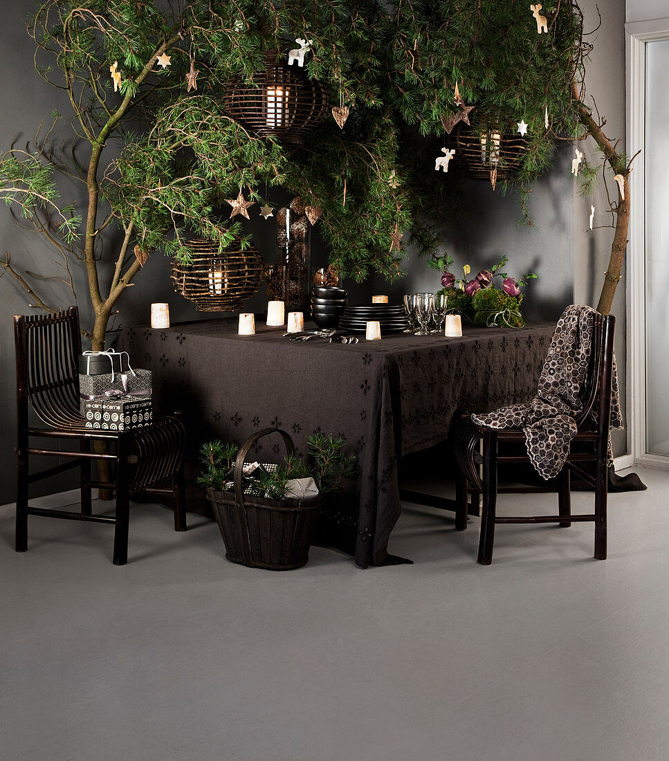 Geschirr und Kerzen auf brauner Tischdecke unter weihnachtlich dekoriert Ästen