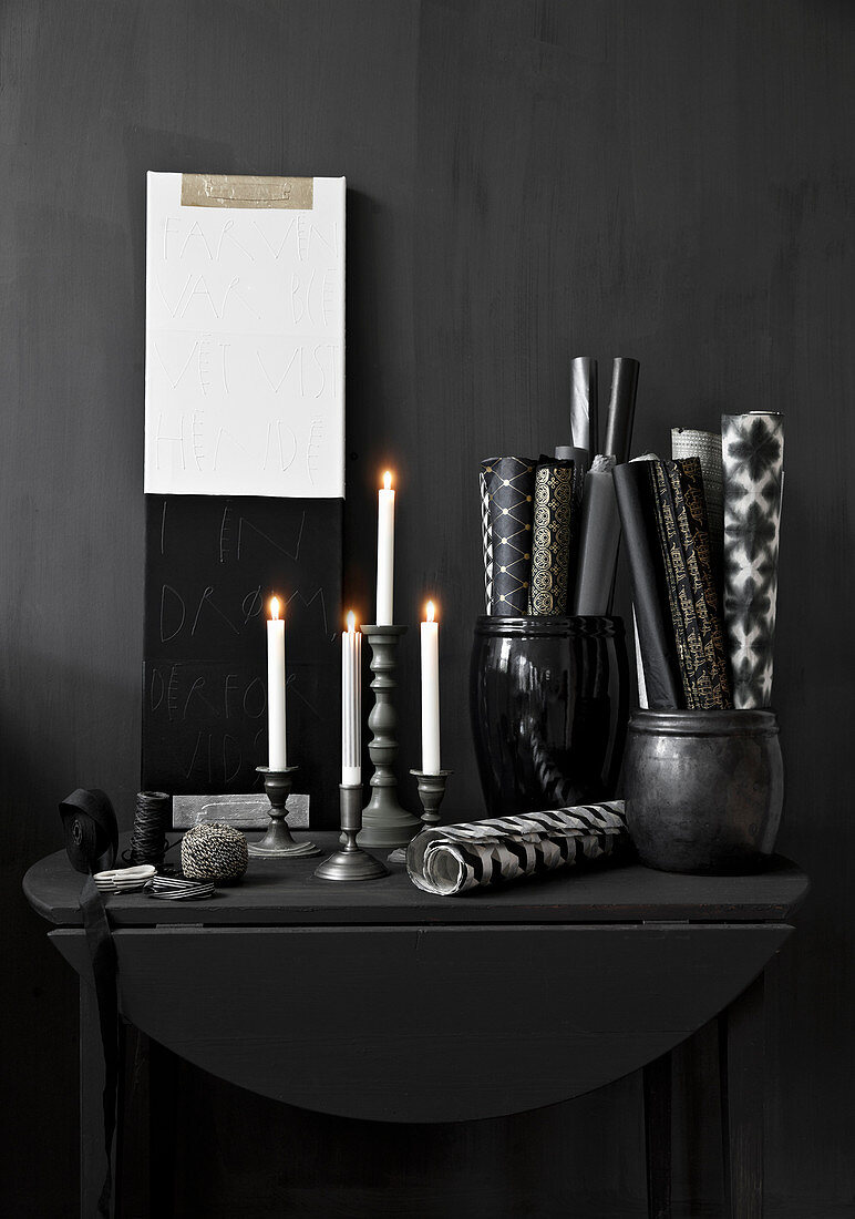 Lit candles and rolls of paper in containers on black console table