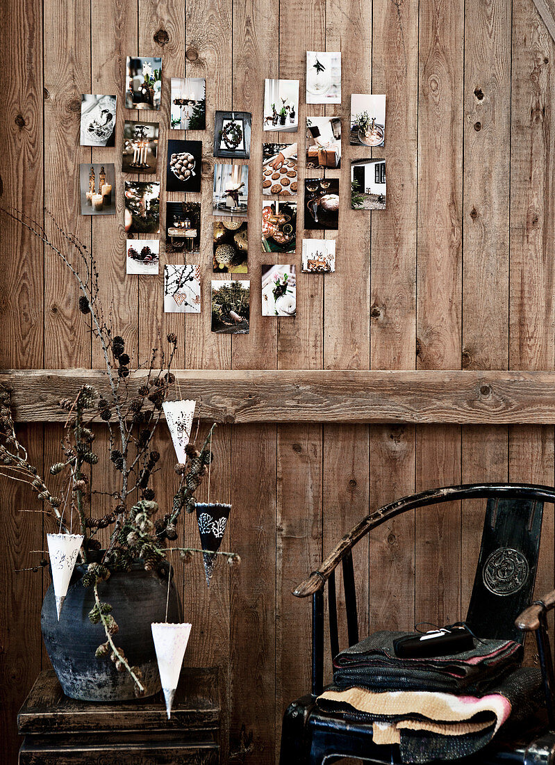 Alte Fotos in Herzform arrangiert an rustikaler Bretterwand, darunter Stuhl und Beistelltisch