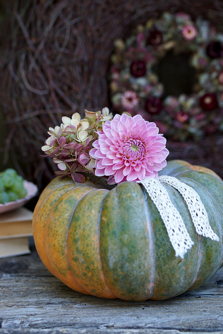 Dahlia and hydrangea flowers with lace ribbon on top of pumpkin