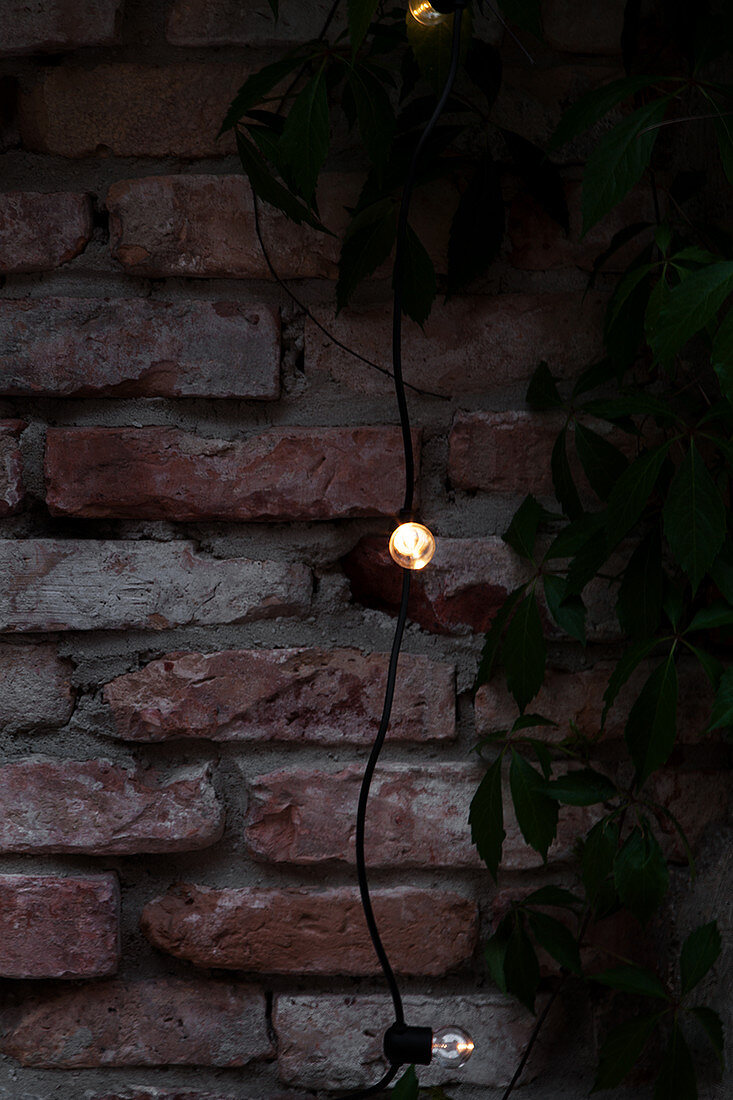 Lichterkette vor Ziegelwand auf der Terrasse