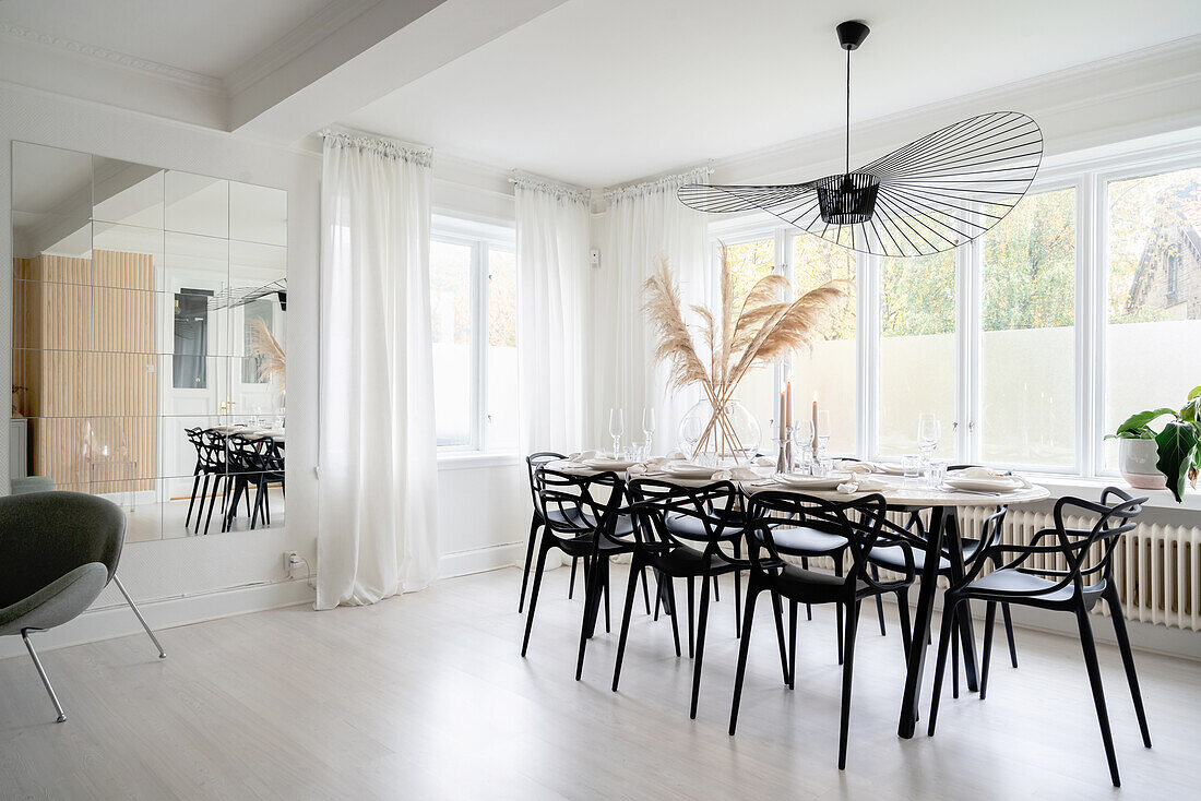 Bright dining area with black chairs, with a designer lamp hanging from above in front of window