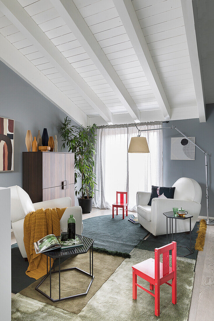 Weiße Ledersessel, Beistelltisch, rote Kinderstühle und verschiedene Teppiche im Wohnzimmer