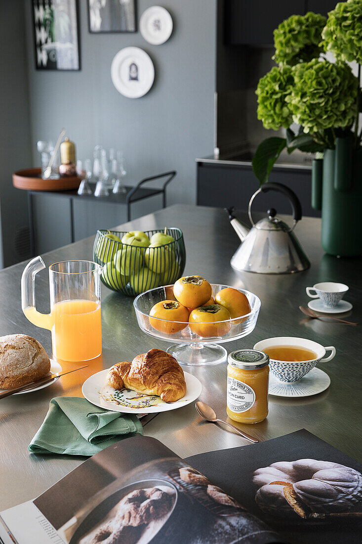 Gedeckter Frühstückstisch mit Croissant, Marmelade, Tee, Obst und Saft