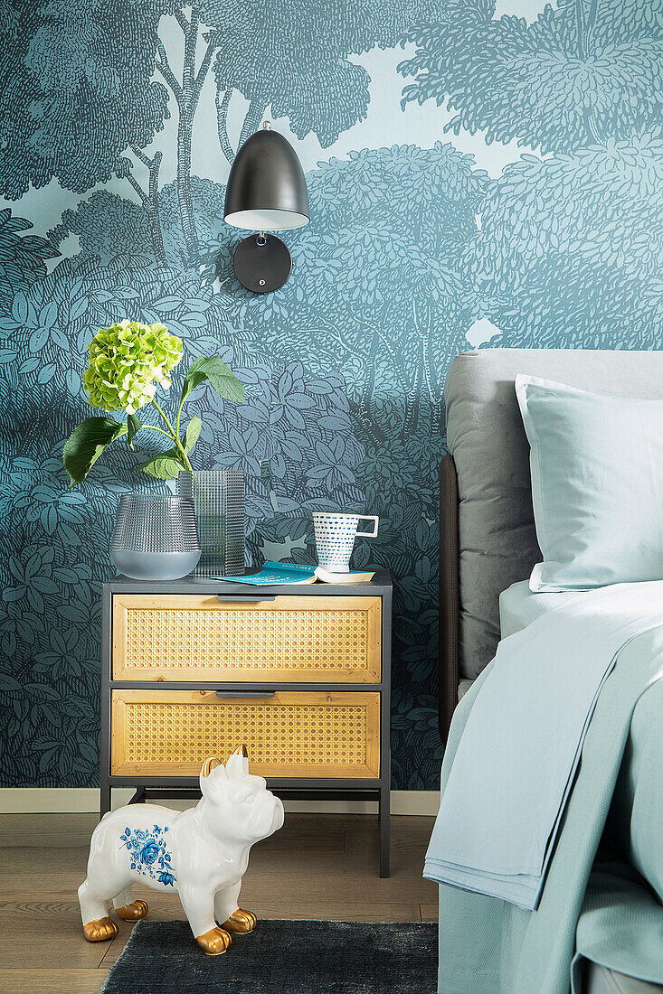 Nightstand with Viennese cane weave in front of forest wallpaper and ceramic dog figurine in the bedroom