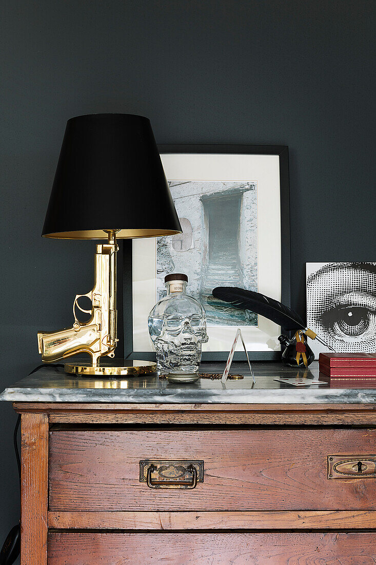 Golden revolver lamp on old wooden dresser in front of black wall