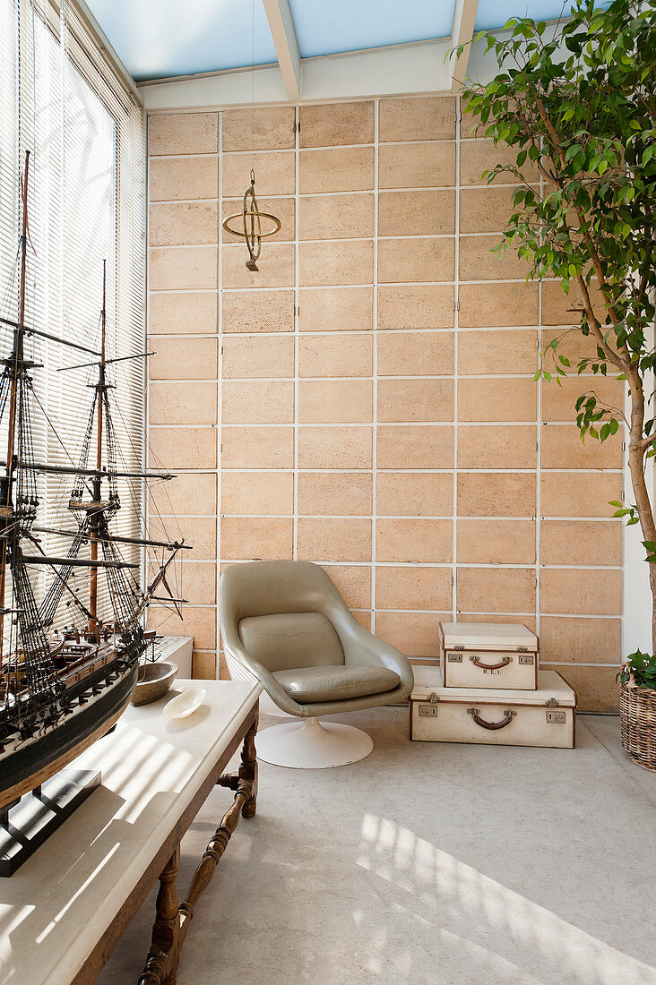 Leather chair in conservatory with terracotta wall tiles and model boat in foreground