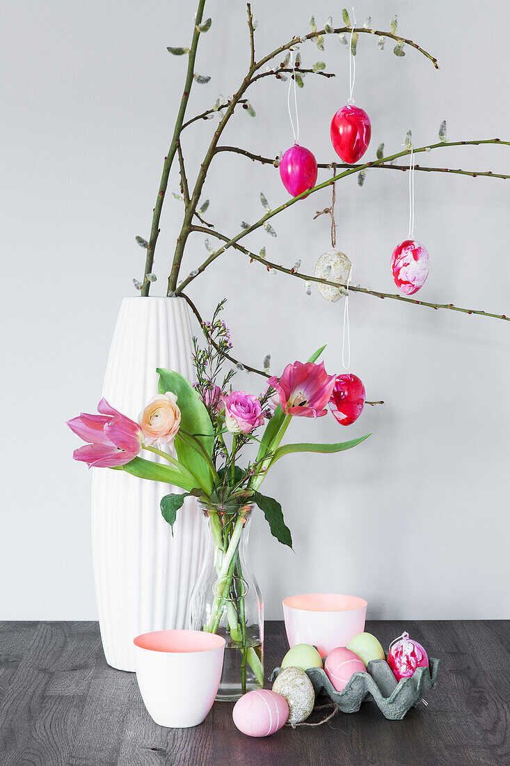 Zweige mit marmorierten Ostereiern in weißer Vase, davor Glasvase mit Tulpen
