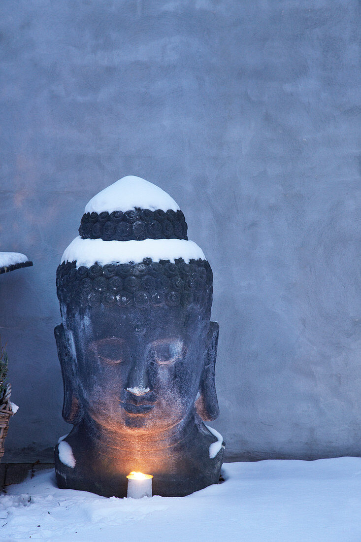 Mit Kerze beleuchteter Buddhakopf im Schnee