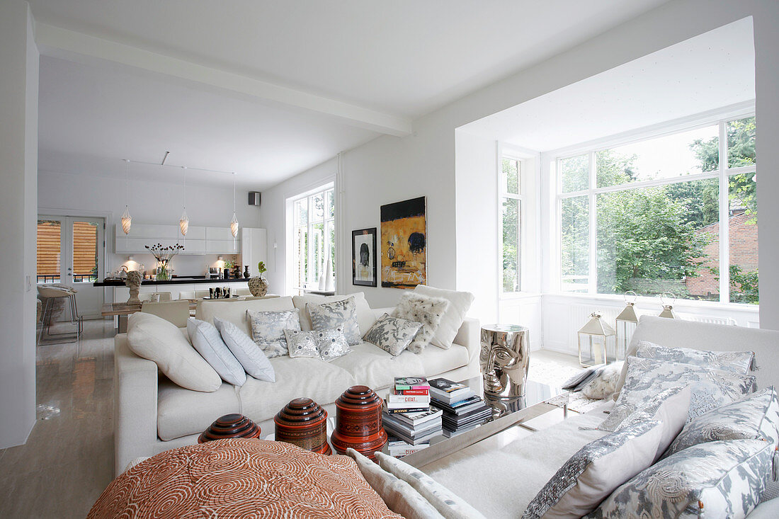 White sofas with scatter cushions next to window in open-plan interior