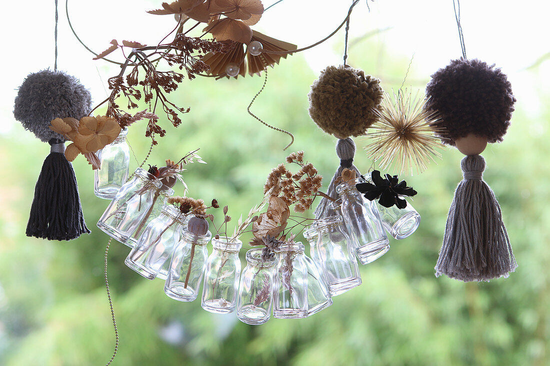 Handmade garland made from miniature glass bottles holding dried grasses and pompoms with tassels