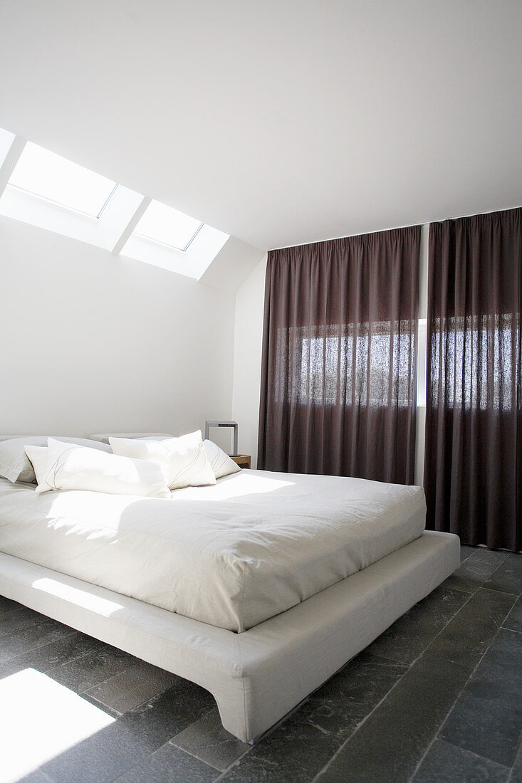 Double bed with white bed linen in bedroom with skylight