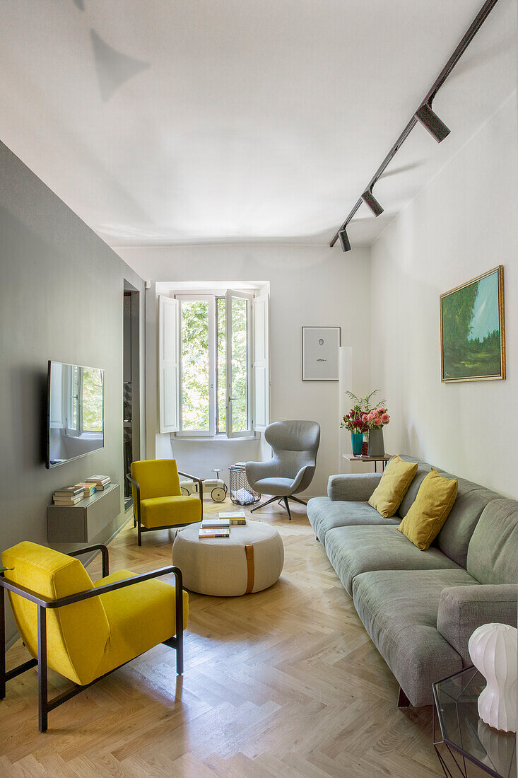 Gelbe Sessel, Couchtisch und graues Sofa in schmalem Wohnzimmer