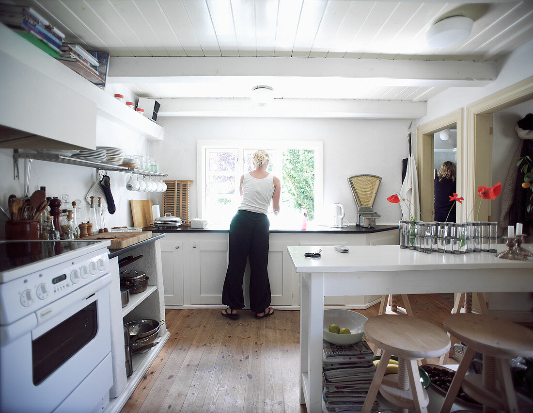 Woman in kitchen-dining room with white cabinets and black worksurfaces