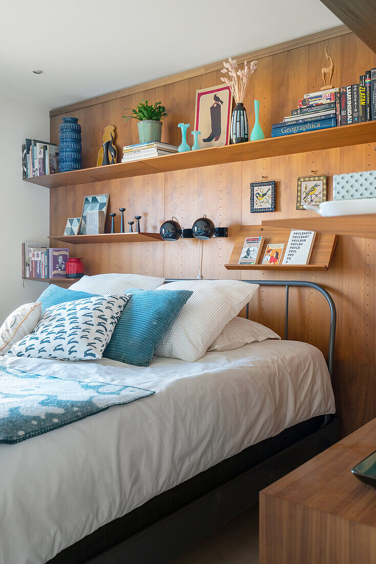Shelves on wooden wall above double bed in bedroom