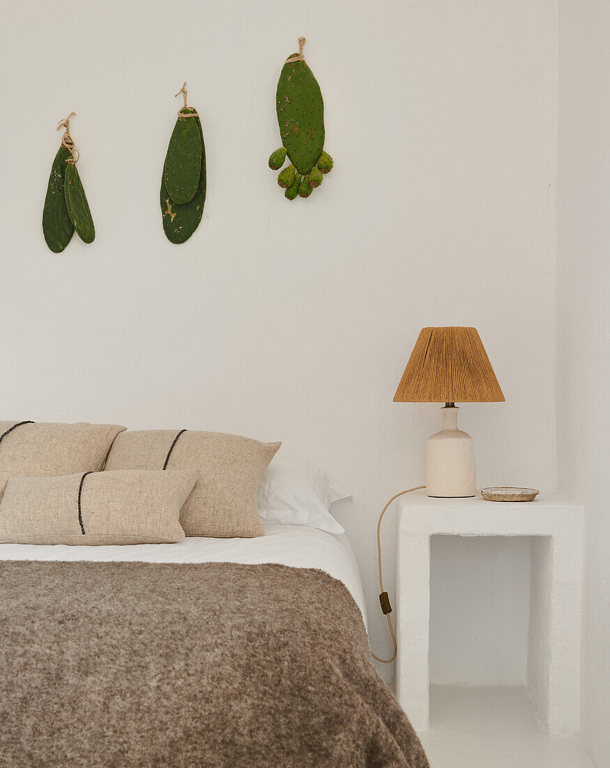Bed and bedside table in front of white wall with cacti branches